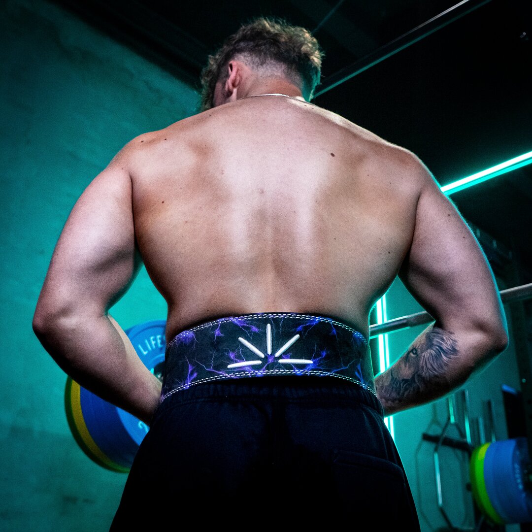 En mand iført lilla Trackfie træningsbælte står med ryggen til i et fitnesscenter