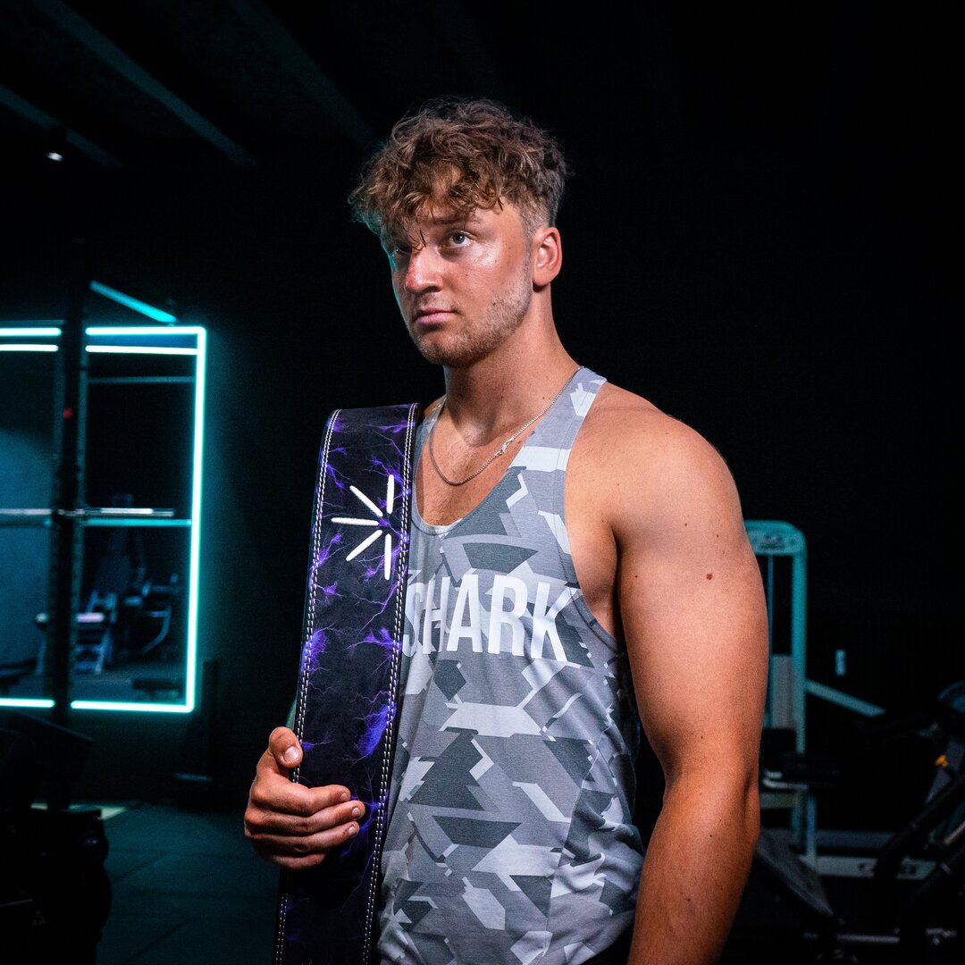 En mand med lilla Trackfie træningsbælte over skulderen står nede i fitnesscenter