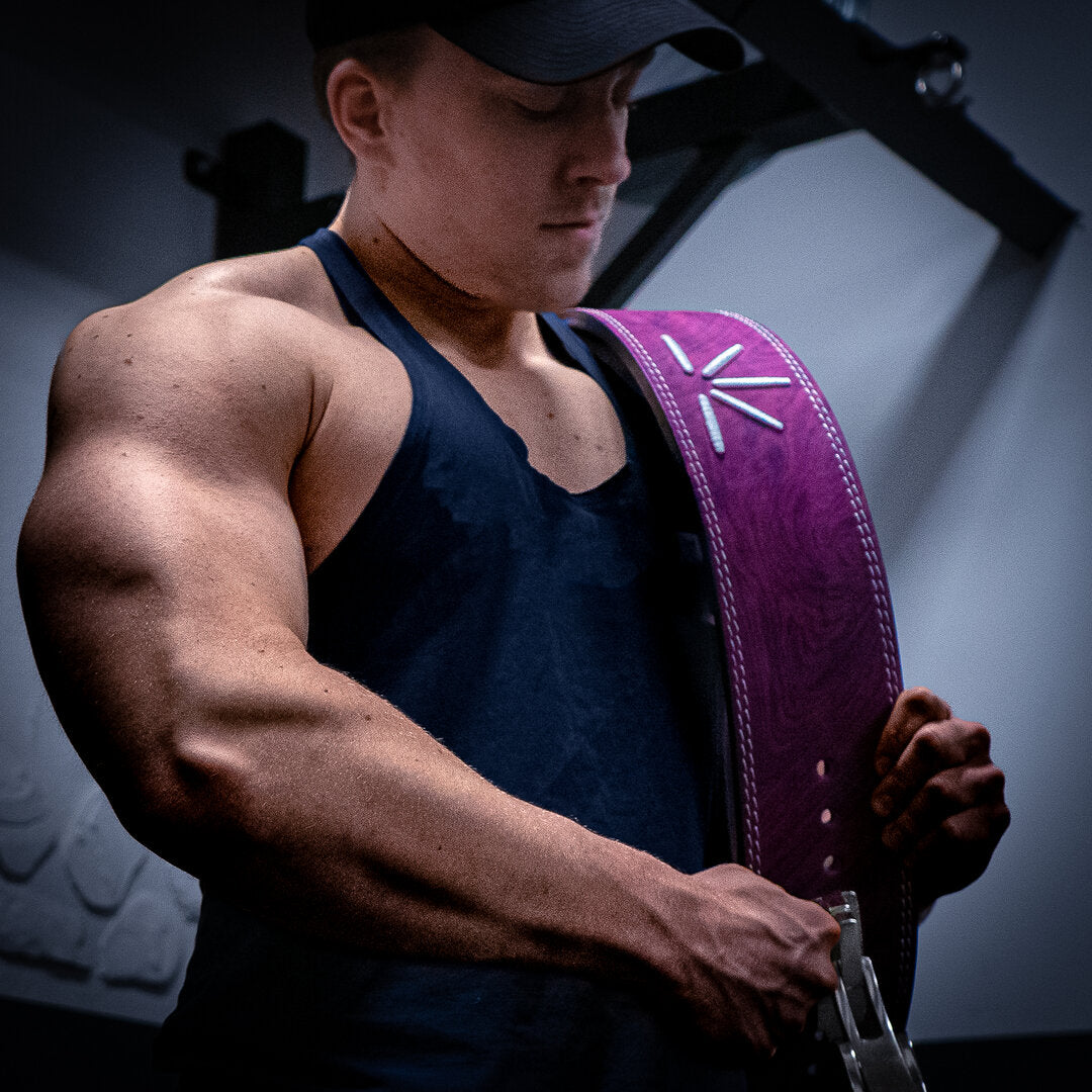 En mand med lilla Trackfie træningsbælte over skulderen står nede i fitnesscenter